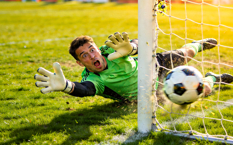 足球场上守门员扑救失误后一脸囧态，皮球滚入网窝